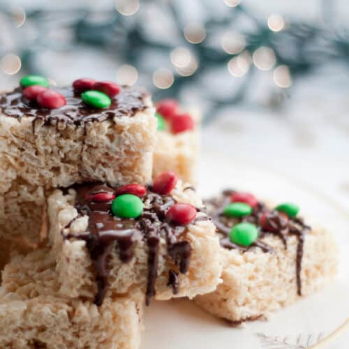 Stack of Rice Krispy Treats decorated for Christmas on a plate with Christmas lights in background.