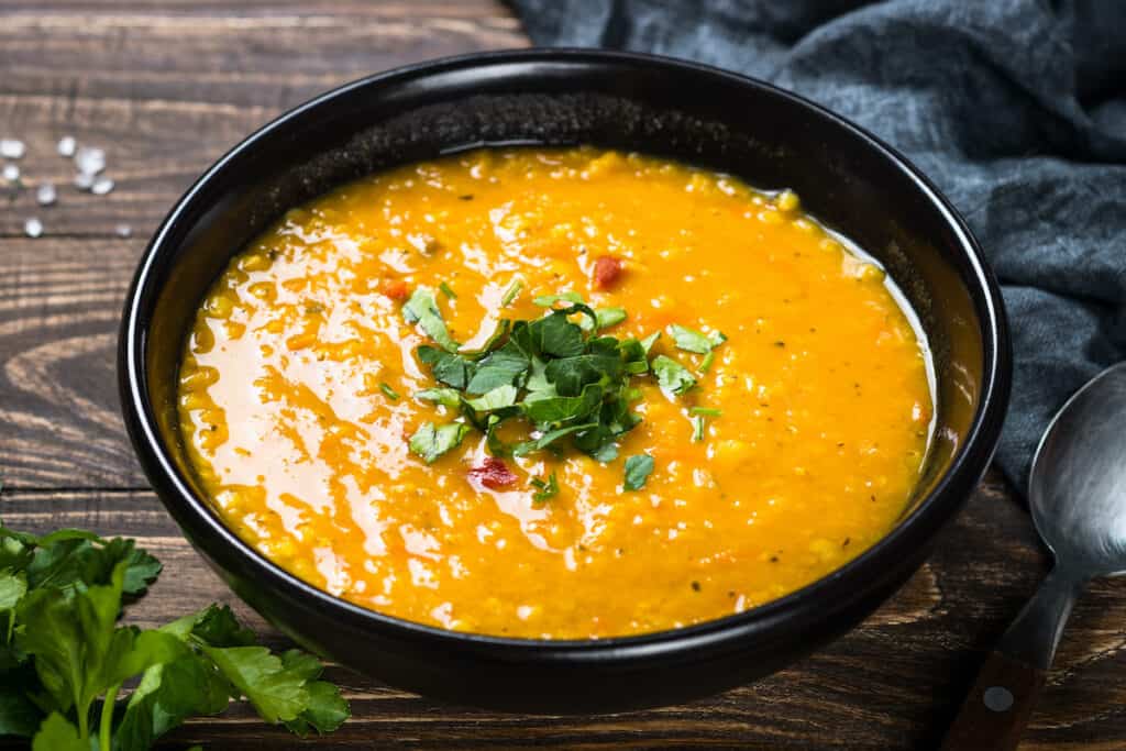 Red lentil soup puree in black plate on wooden table.