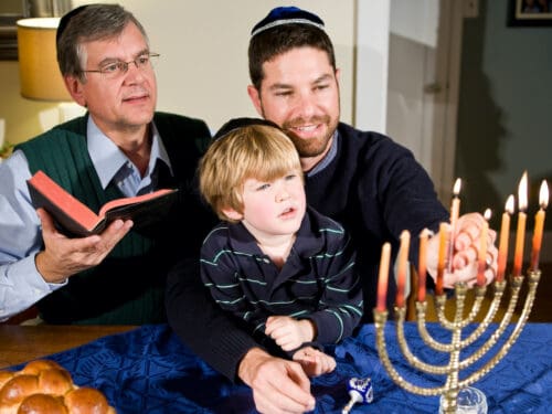 Four year old boy with grandfather and father lighting Hanukkah menorah