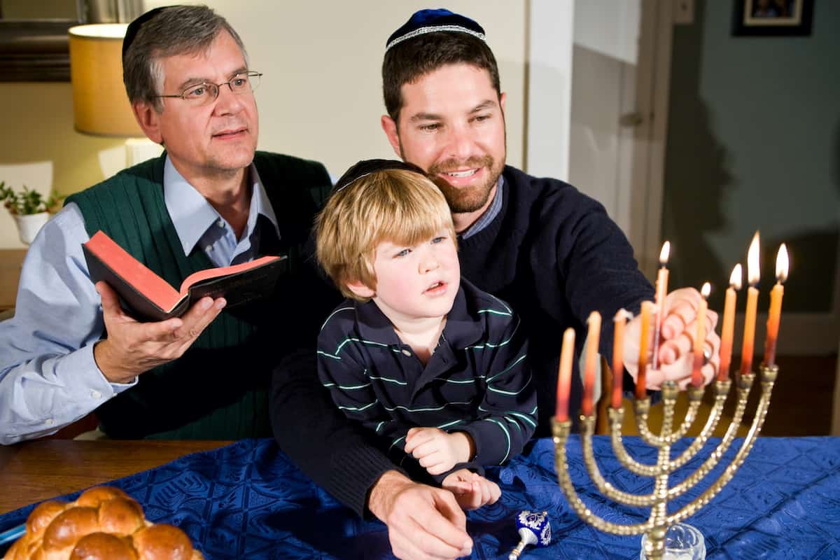 Four year old boy with grandfather and father lighting Hanukkah menorah